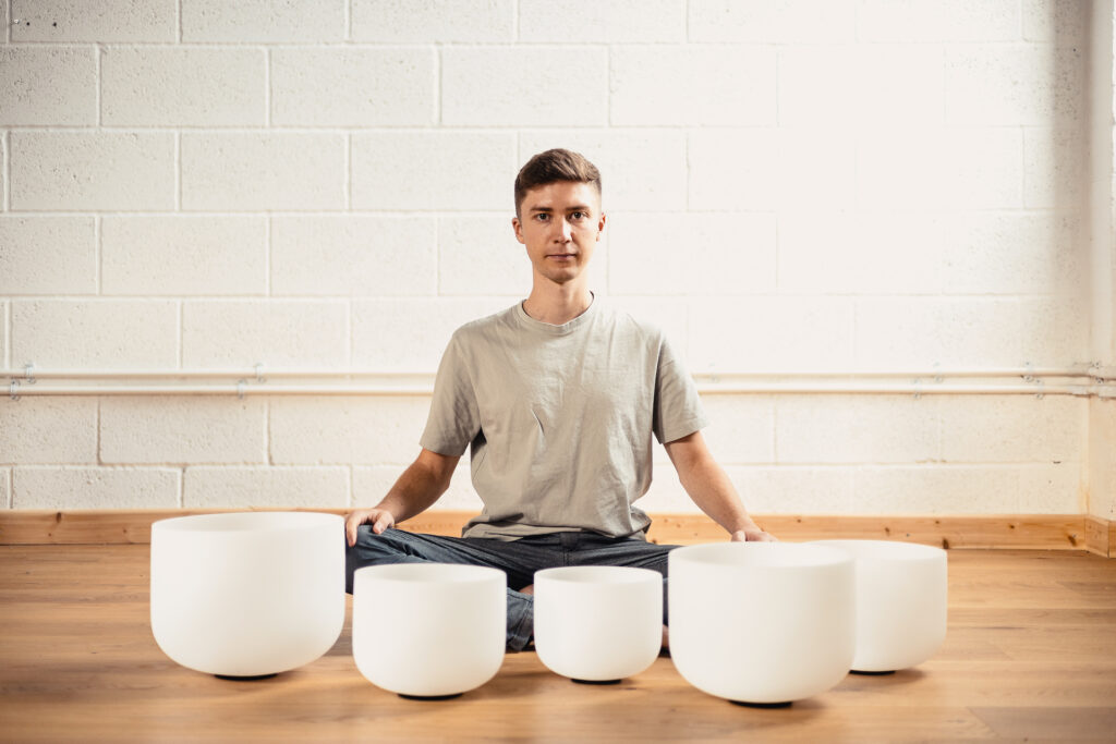 Sound healer Noah Kempf playing singing bowls in a healing session with warm atmospheric lighting